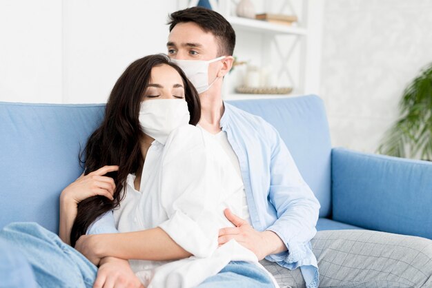 Couple with face masks embraced on sofa