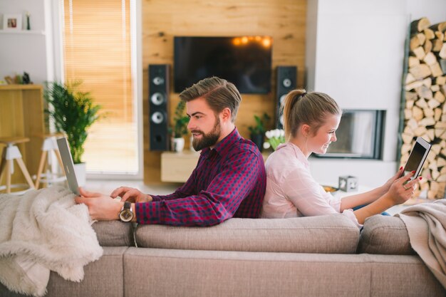 Couple with gadgets sitting on couch