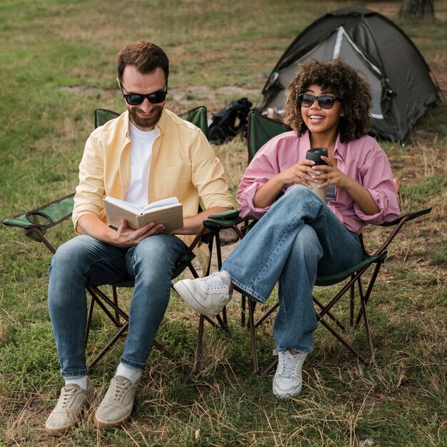 Couple with sunglasses reading and drinking while camping outdoors