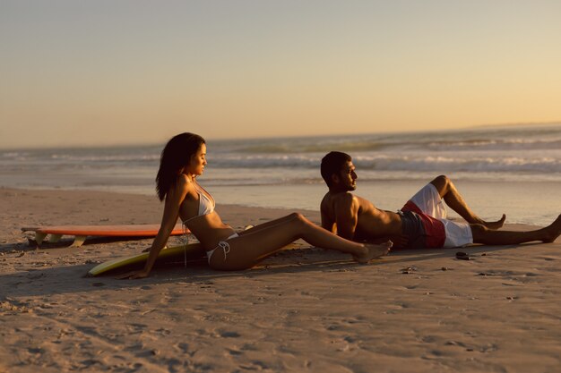 Couple with surfboard relaxing on the beach at dusk