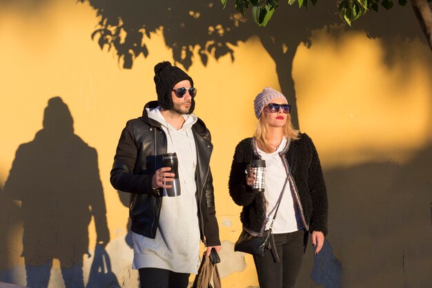 Couple with thermoses standing near wall