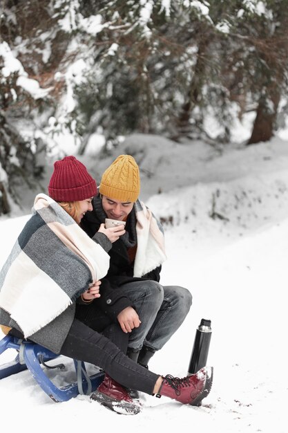Couple with winter clothes sitting on sleigh and drink tea