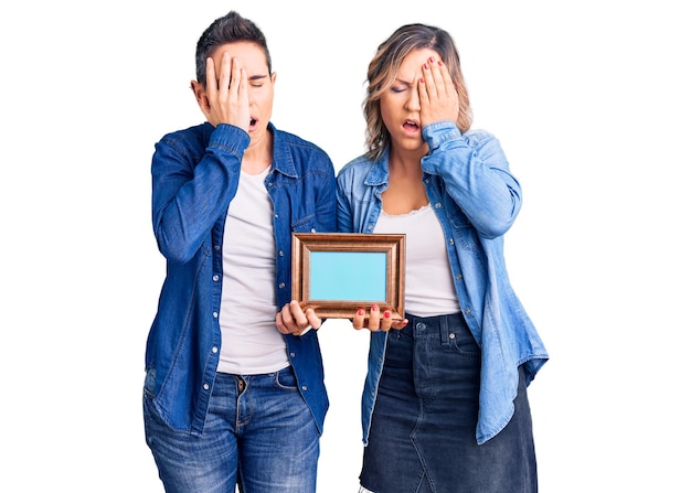 Couple of women holding empty frame yawning tired covering half face, eye and mouth with hand. face hurts in pain.