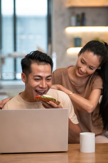 Couple working at home on laptop while having sandwich and coffee