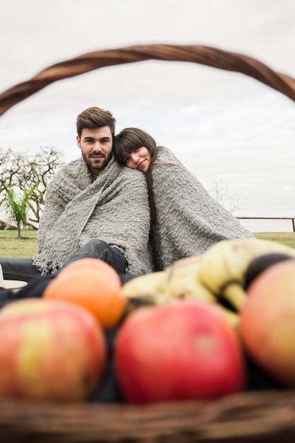 無料写真 果物のバスケットの前に座っている一枚の毛布で包まれたカップル
