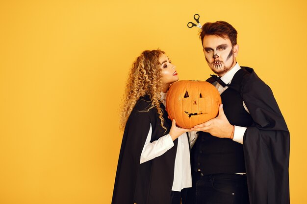 Couple on a yellow background. Woman wearing black costume. Lady with halloween makeup.