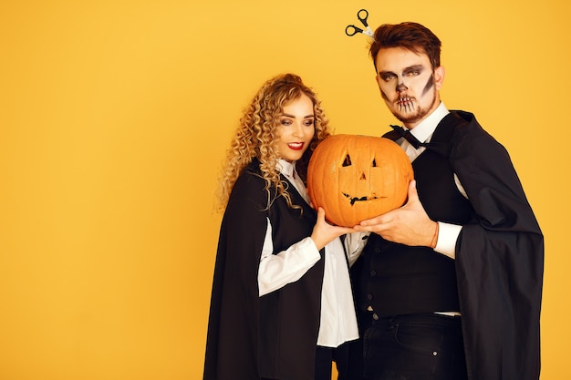 Couple on a yellow background. Woman wearing black costume. Lady with halloween makeup.