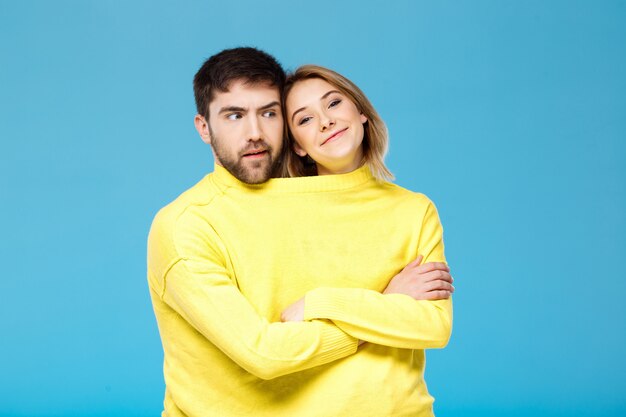 Couple in yellow sweater posing with crossed arms over blue wall