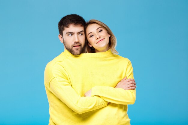 黄色のセーターが青い壁に組んだ腕でポーズのカップル
