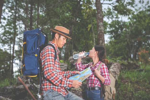 Couples drink water and see a map in the tropical forest along with backpacks in the forest. Adventure, traveling, climbing, hike.