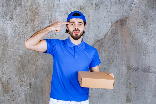 Courier in blue uniform holding a takeaway box and looks confused or having a new idea. 