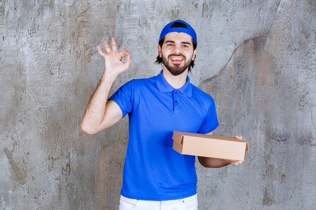 Courier in blue uniform holding a takeaway box and showing positive hand sign.