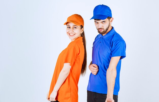 Free photo courier boy and girl in blue and yellow uniforms giving lovely and cheerful poses.