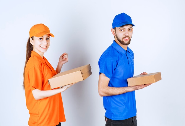 Курьер мальчик и девочка в синей и желтой униформе держат картонные коробки для еды на вынос и пакеты для покупок.