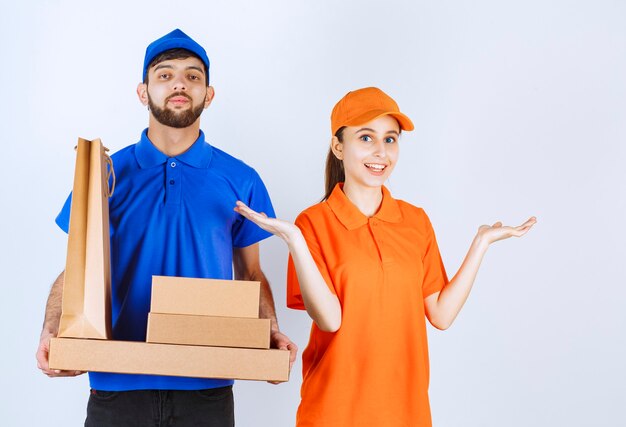 Курьер мальчик и девочка в синей и желтой униформе держат картонные коробки для еды на вынос и пакеты для покупок.
