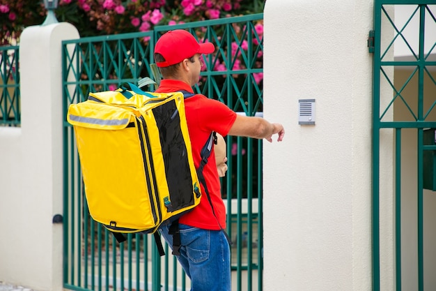 Courier in uniform with isothermal food backpack and package ringing doorbell. Shipping or delivery service concept