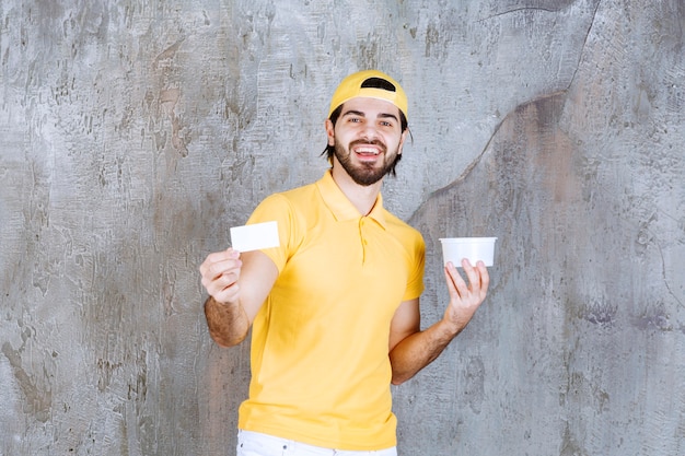 Courier in yellow uniform holding a plastic cup and introducing his business card