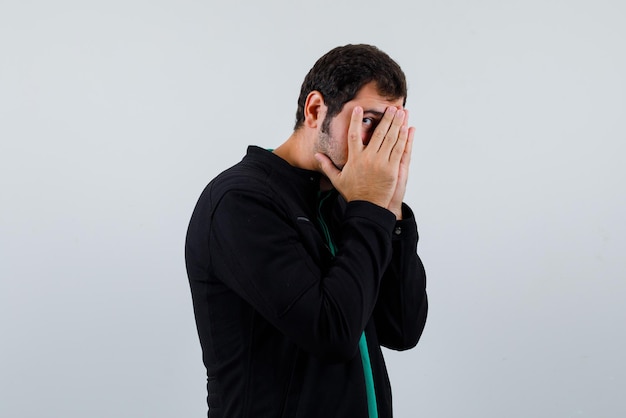 The covered face with hands man is peeking through fingers on white background