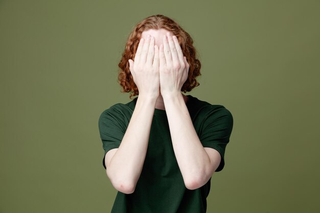 Covered face with hands young handsome guy wearing green t shirt isolated on green background