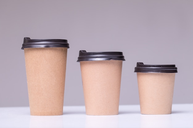 Покрытые бумажные кофейные чашки разных размеров, изолированные на сером