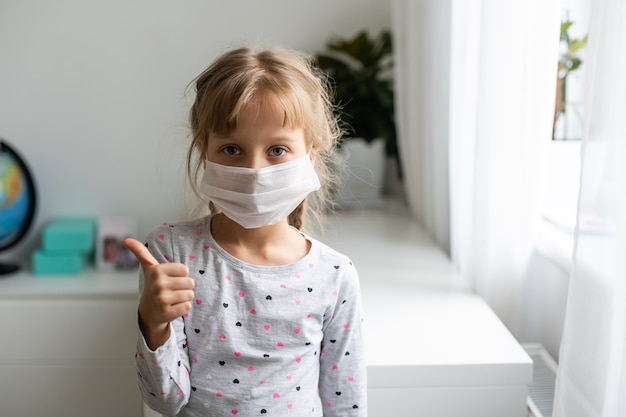 코비드-19와 대기 오염 pm2.5 개념. pm2.5를 보호하기 위해 마스크를 쓴 어린 소녀와 코로나 바이러스 발병을 막기 위한 ok 손가락 손 제스처.