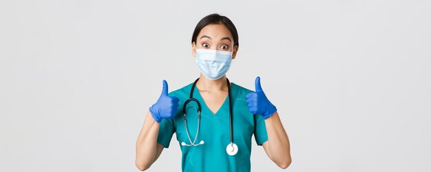 코비드-19, 코로나바이러스 질병, 의료 종사자 개념. 웃고 있는 아시아 의사, 의료 마스크와 고무 장갑을 끼고 엄지손가락을 치켜드는 의사, 승인, 좋은 일 칭찬