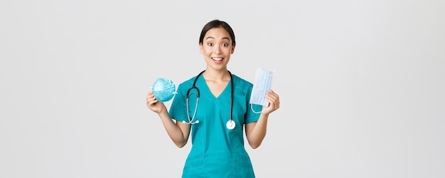 Covid-19、コロナウイルス病、医療従事者の概念。面白がって笑っているアジアの女性看護師、呼吸器と医療用マスクを見せているスクラブのインターは、個人用保護具を受け取ります。