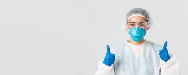 Covid-19, coronavirus disease, healthcare workers concept. Close-up of confident professional female asian doctor, tech lab employee in personal protective equipment show thumbs-up in approval.
