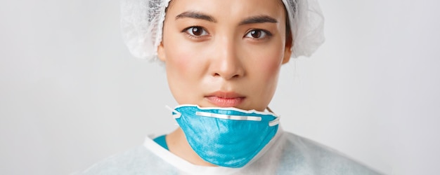 Free photo covid-19, coronavirus disease, healthcare workers concept. close-up of exhausted serious-looking asian female doctor take-off personal protective equipment, have skin damage from respirator.