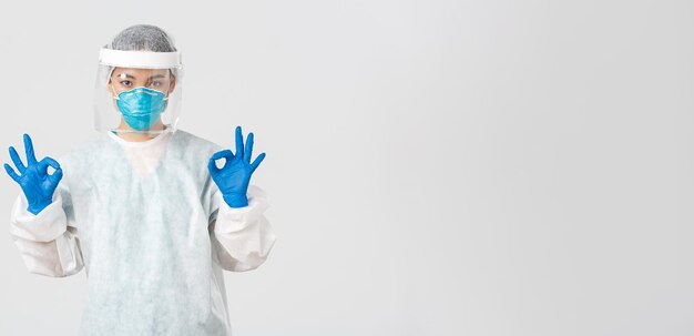 Covid-19, coronavirus disease, healthcare workers concept. Confident and serious asian female doctor, lab technician in personal protective equipment showing okay gesture in approval