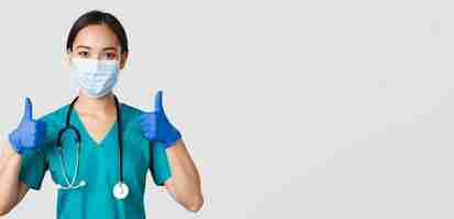 Free photo covid-19, coronavirus disease, healthcare workers concept. confident smiling asian doctor, nurse in medical mask and rubber gloves, show thumbs-up in approval, provide service, wite background