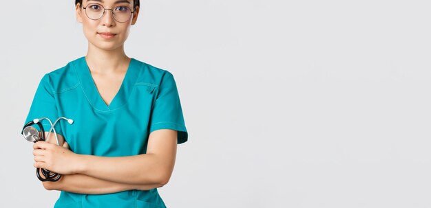 Covid-19, coronavirus disease, healthcare workers concept. Confident smiling professional asian doctor in glasses, cross arms chest, wearing scrubs and holding stethoscope, white background.