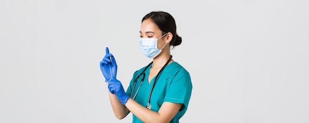 Covid-19、コロナウイルス病、医療従事者の概念。プロの笑顔のアジアの女性看護師、スクラブの医師、医療マスクは、検査、患者の検査のためにゴム手袋を着用します。