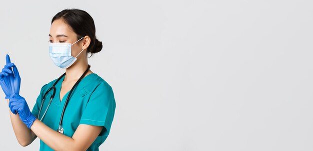 코비드-19, 코로나바이러스 질병, 의료 종사자 개념. 웃고 있는 전문 아시아 여성 간호사, 수술용 의사, 의료용 마스크를 착용하고 검진, 환자 검사를 위해 고무 장갑을 끼고 있습니다.