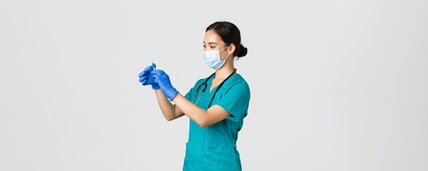 Covid-19, coronavirus disease, healthcare workers concept. Profile of asian female doctor, nurse in medical mask and globes, fill syringe with vaccine, doing vaccination shots, white background.