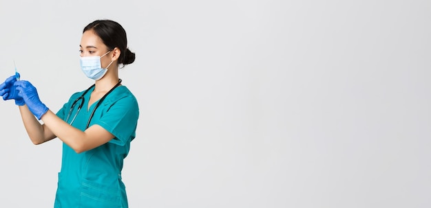 Free photo covid-19, coronavirus disease, healthcare workers concept. profile of asian female doctor, nurse in medical mask and globes, fill syringe with vaccine, doing vaccination shots, white background.