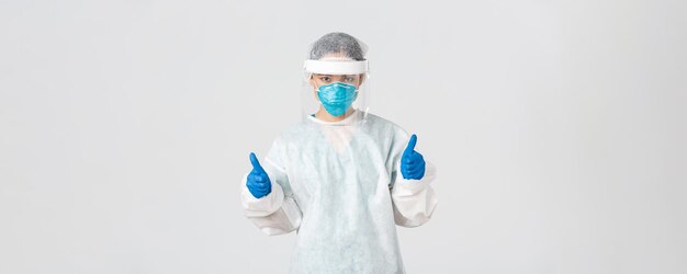 Covid-19, coronavirus disease, healthcare workers concept. Serious-looking confident young asian female doctor, infectionist in personal protective equipment showing thumbs-up, enter dangerious zone.