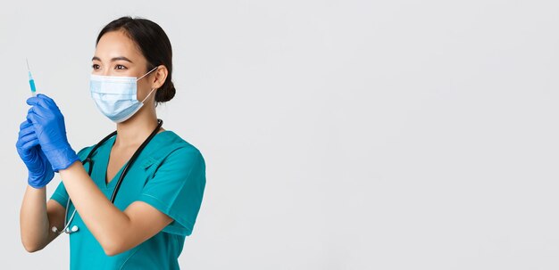 Covid-19, coronavirus disease, healthcare workers concept. Side view of confident smiling asian female physician, nurse prepare syringe with vaccine for flu shot, standing white background