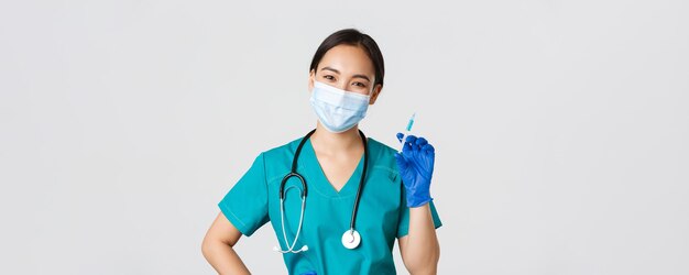 Covid-19, coronavirus disease, healthcare workers concept. Smiling cheerful asian doctor, nurse in medical mask and rubber gloves prepare syringe with vaccine for shot vaccination, white background