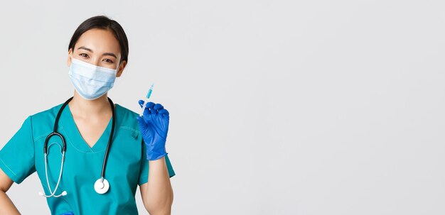 Covid-19, coronavirus disease, healthcare workers concept. Smiling cheerful asian doctor, nurse in medical mask and rubber gloves prepare syringe with vaccine for shot vaccination, white background