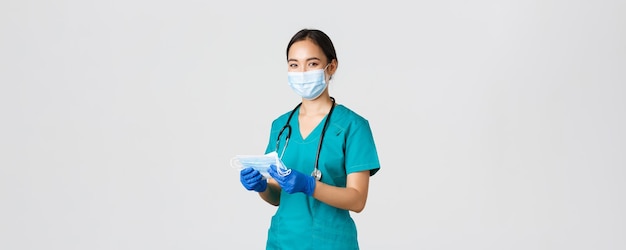 Covid-19、コロナウイルス病、医療従事者の概念。笑顔のフレンドリーな女性看護師、スクラブとゴム手袋の医師は、患者に医療用マスク、白い背景を提供します。