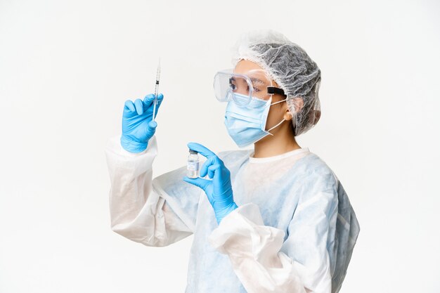Covid-19, коронавирус и концепция кампании вакцинации. Азиатская медсестра или врач в лицевой маске, заполняя шприц вакциной, стоя на белом фоне.