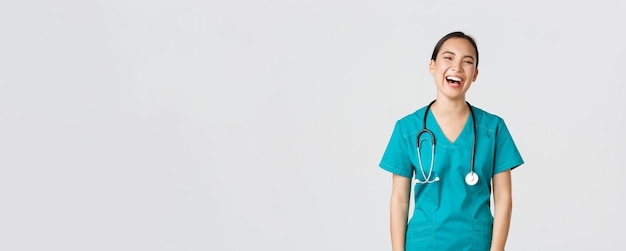 Free Photo covid-19, healthcare workers, pandemic concept. carefree beautiful female asian nurse in scrubs, intern having fun, laughing happy. doctor on lunch break chuckle and talking to coworkers