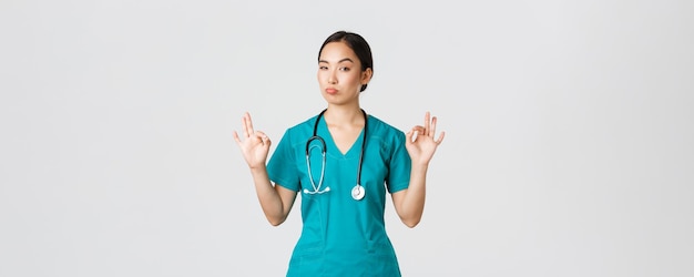Covid-19, медицинские работники, концепция пандемии. Впечатленная красивая азиатская медсестра в халате, доктор показывает хороший жест и кивает в знак одобрения, хвалит отличный выбор, делает комплименты кому-то