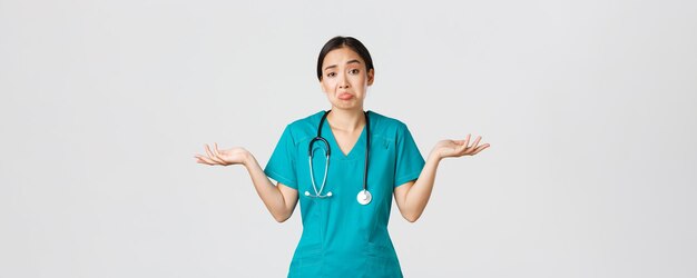 Covid-19、医療従事者、パンデミックの概念。無知なアジアの女性看護師の肖像画、肩をすくめて手を横に広げた女性医師、知らない、助けられない、白い背景。
