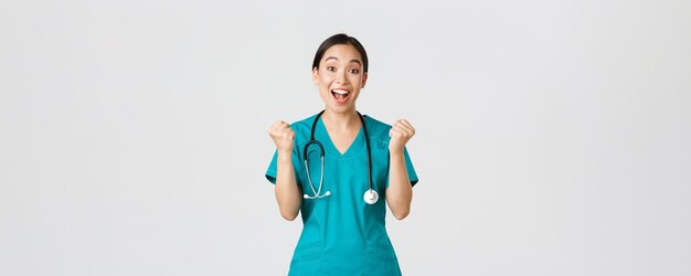 Covid-19, healthcare workers and preventing virus concept. Hopeful and relieved, joyful asian pretty female doctor, physician rejoicing with fists pump, congrats or praise someone, winning