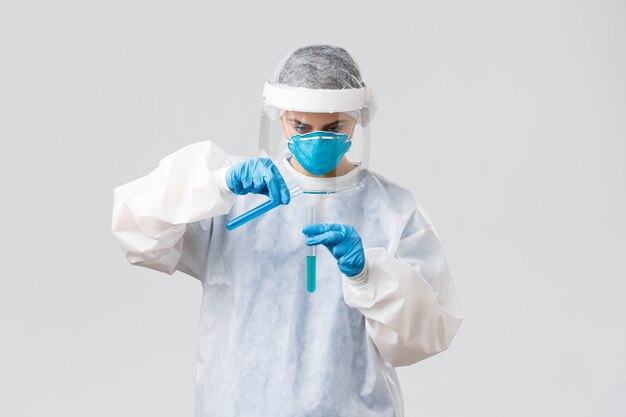 Covid-19, медицинские исследования, медицинские работники и концепция карантина. Врач технической лаборатории в клинике, работающий над вакциной против коронавируса, наливает жидкость в другую пробирку, носит личный защитный костюм
