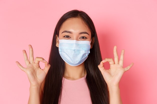 Covid-19 pandemic, coronavirus and social distancing concept. Close-up of excited and amazed pretty asian girl praise great choice, well done or good job gesture, show okay and wear medical mask