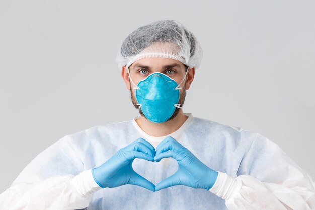 Covid-19, pandemic, healthcare workers fighting virus outbreak. Doctor in personal protective equipment, medical respirator and rubber gloves, showing heart sign, stay strong during coronavirus