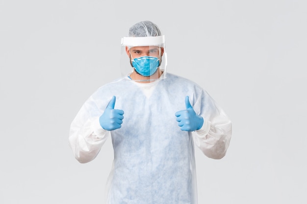 Free photo covid-19 pandemic, virus outbreak, clinic and healthcare workers concept. supportive doctor in personal protective equipment, show thumbs-up, encourage medical personnel do their best